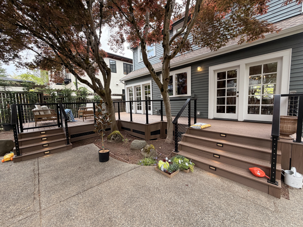 Olympic Decks Multi-Level Composite Deck Featuring Black Cable Railings, Built-In Stair Lights, And A Mature Japanese Maple Tree.